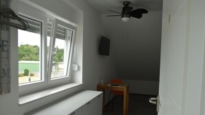 Een kamer met raam, plafondventilator, bureau en stoel.
