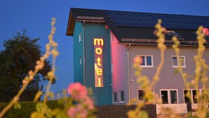 Een motel met een opvallend neonbord, zonnepanelen op het dak en een bord met tekst.