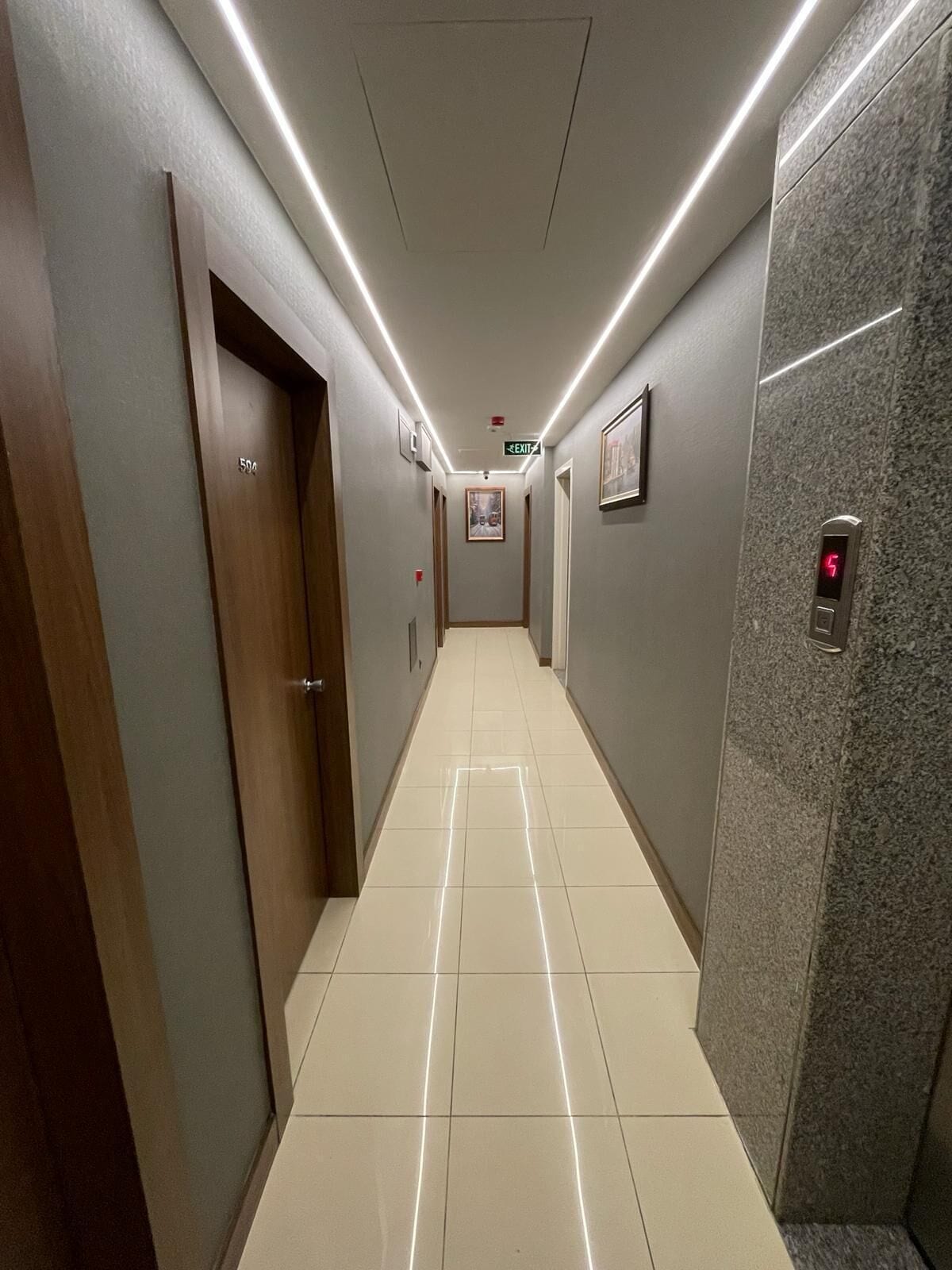 A hallway with a tiled floor, wooden doors, and a marble wall.