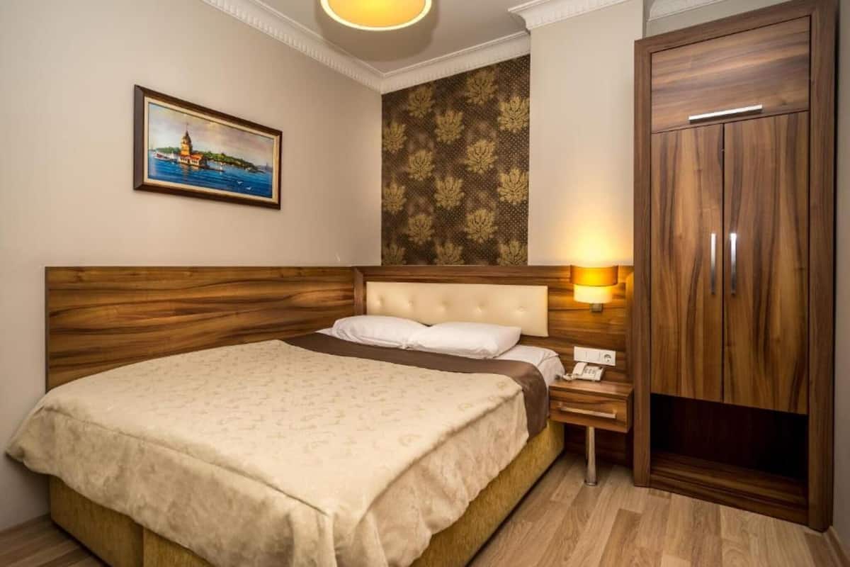 Une chambre d’hôtel avec un lit, une table de chevet, une lampe, une armoire et un tableau au mur.