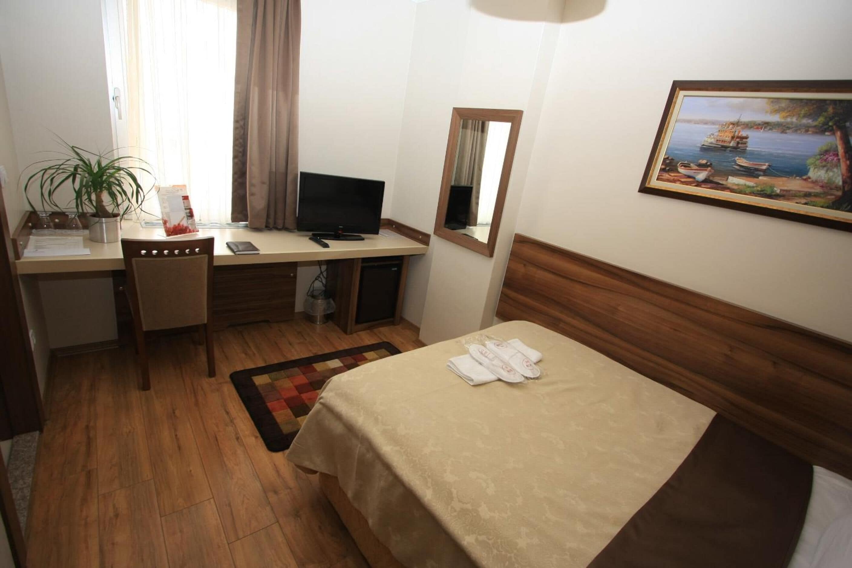 A hotel room with a bed, desk, chair, television, and a painting on the wall.
