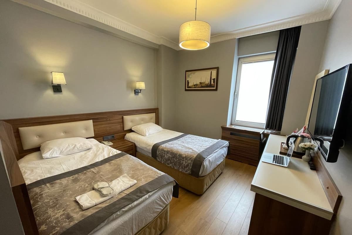 Une chambre d’hôtel avec deux lits, un bureau avec un ordinateur portable, une télévision et une fenêtre avec des rideaux.