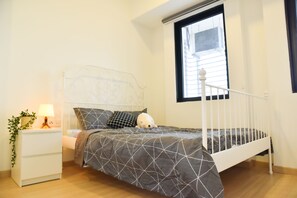 A bedroom with a bed, a nightstand, a lamp, and a window.