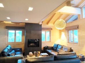 Ein modernes Wohnzimmer mit Ledersofas, einem Kamin und großen Fenstern.
