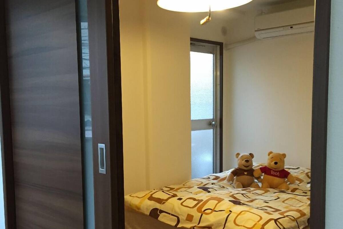 A bedroom with a bed, two teddy bears, a window, and a ceiling light.