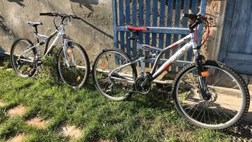 Due biciclette parcheggiate su un prato di fronte a un edificio con una recinzione blu e una finestra con persiane blu.