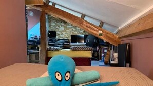 A bedroom with a bed, a blue octopus plush toy, and a stone wall in the background. - Chambres Bambou & Corail & Music (Saint Sever)