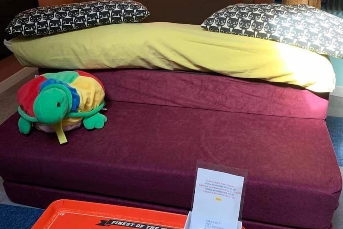 A small, cozy room with a bed, a plush toy, and a coffee box on the floor.