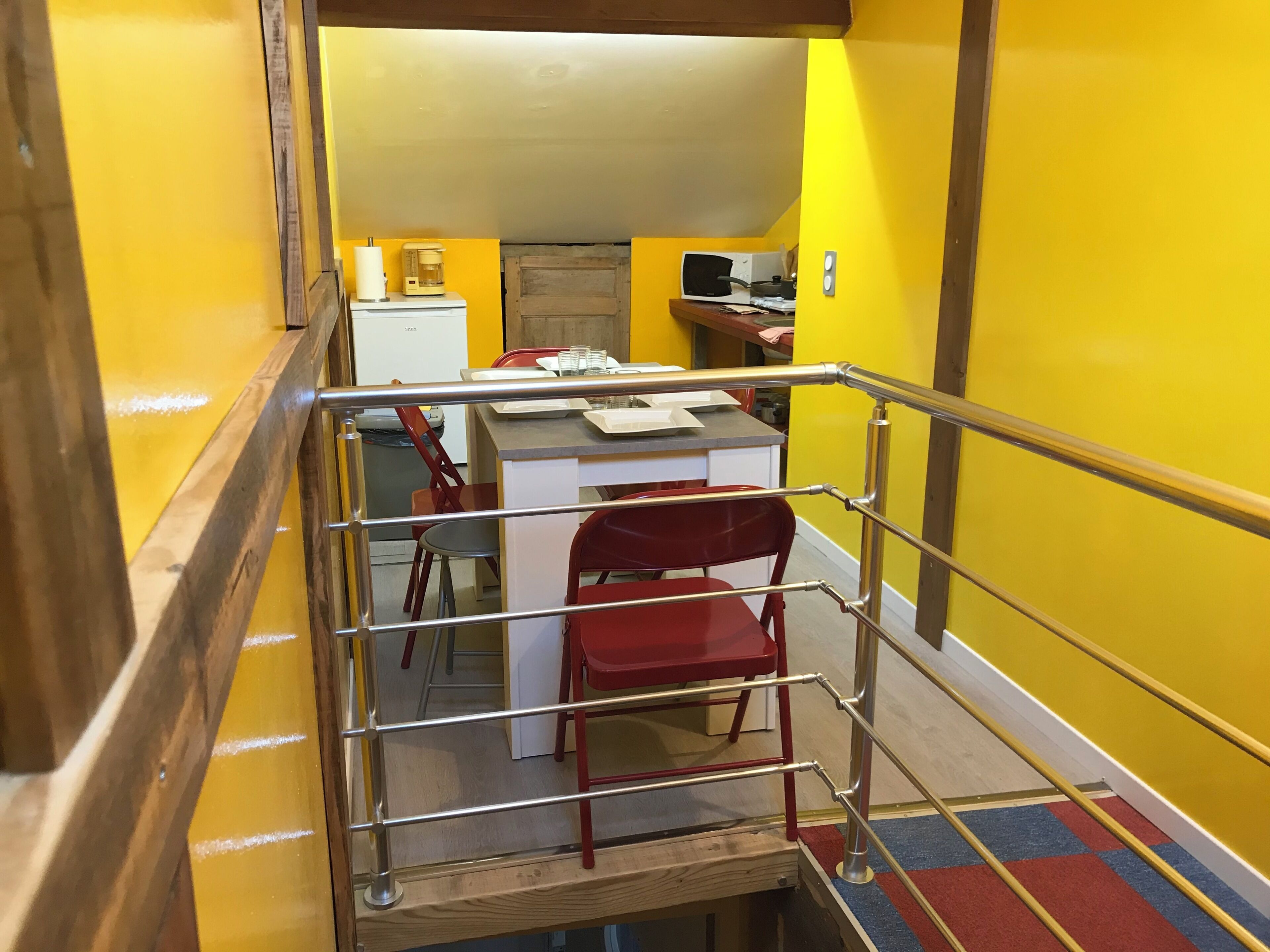 A staircase with a metal railing leading to a room with a desk, chairs, and a coffee maker.