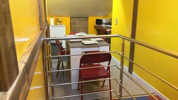 A staircase with a metal railing leading to a room with a desk, chairs, and a coffee maker.
