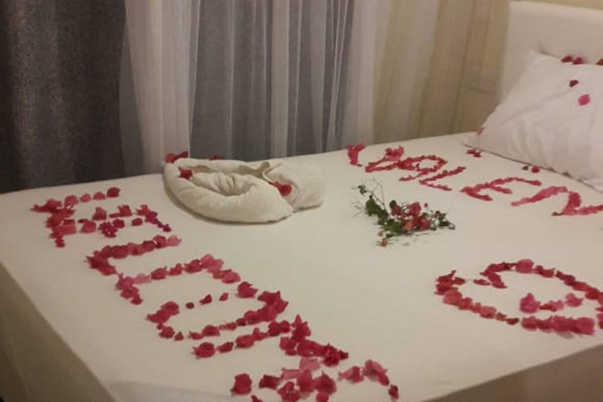 A bed with rose petals arranged in a heart shape and the word "LOVE" spelled out.