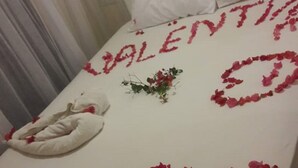 A bed with a white sheet and pillows, decorated with red rose petals spelling "Valentine's Day" and "Welcome".