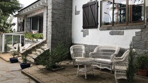 A stone house with a porch, wicker furniture, and potted plants.