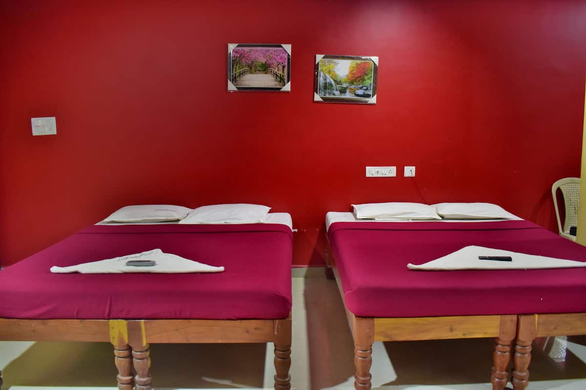 Two single beds with red bedding, wooden frames, and white pillows. There are two small framed pictures on the red wall.