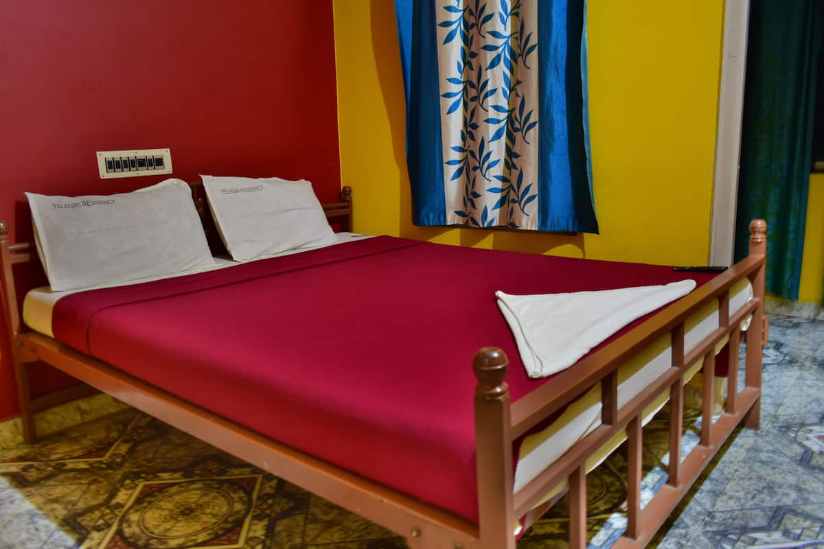 A single-bed room with a wooden frame, a red bedspread, and two pillows.