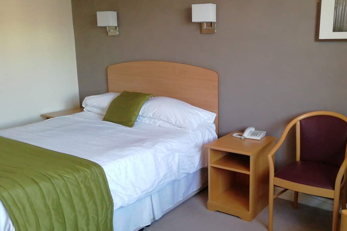 Une chambre d’hôtel comprenant un lit, un bureau avec un téléphone, une chaise et deux lampes fixées au mur.