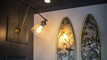 Een muur met twee ovale decoratieve panelen met vogel- en boommotieven, een moderne hanglamp en een lijst met een foto boven een deur.