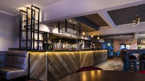 Una zona de bar con mostrador de madera, asientos con sillas acolchadas y un techo alto con vigas a la vista.