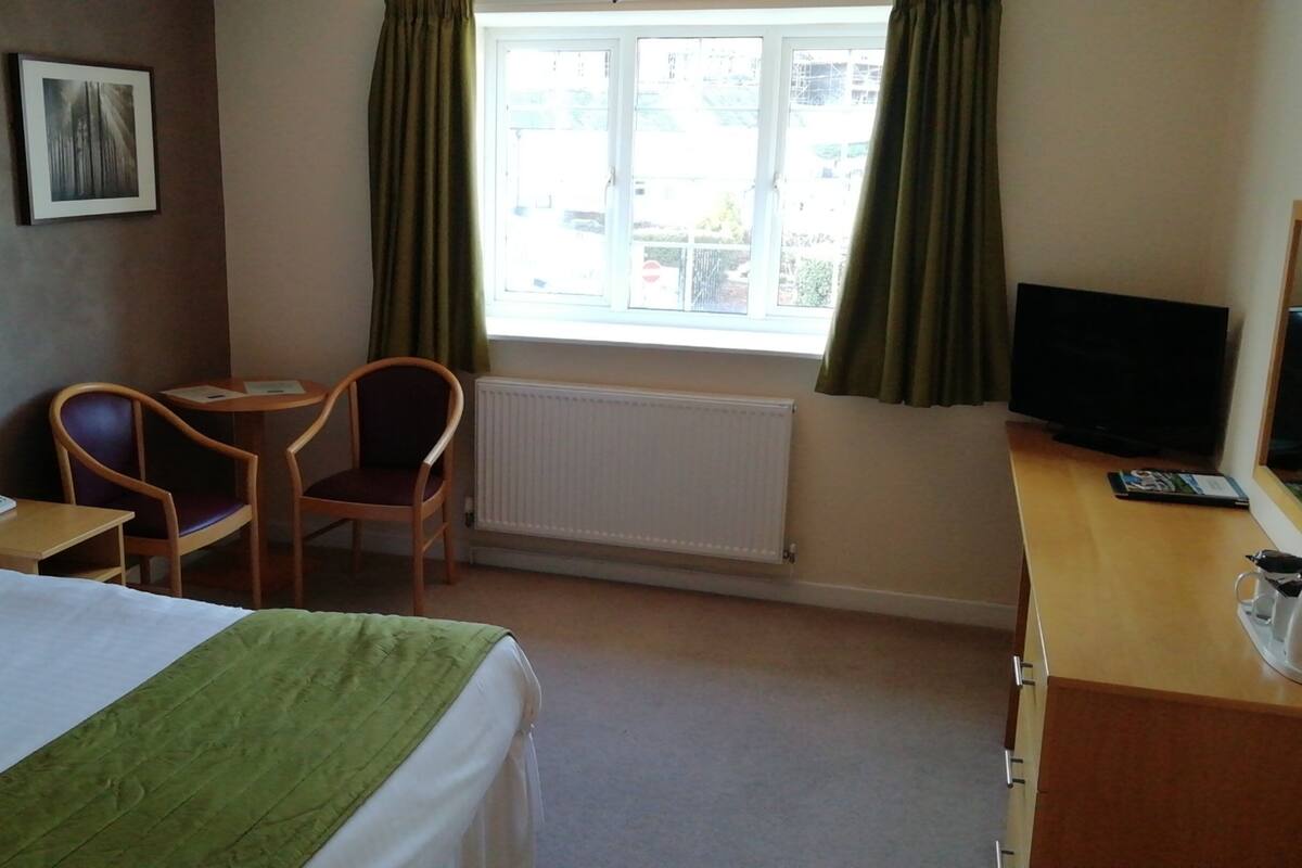 Une chambre d’hôtel avec un lit, un bureau, une chaise, une télévision et une fenêtre avec des rideaux.
