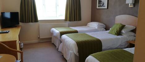 A hotel room with two single beds, a desk with a television, a radiator, and a window with curtains.