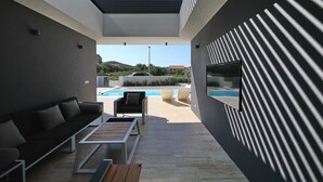 Un espacio exterior moderno con piscina, sofá, mesa de centro y televisor en la pared.