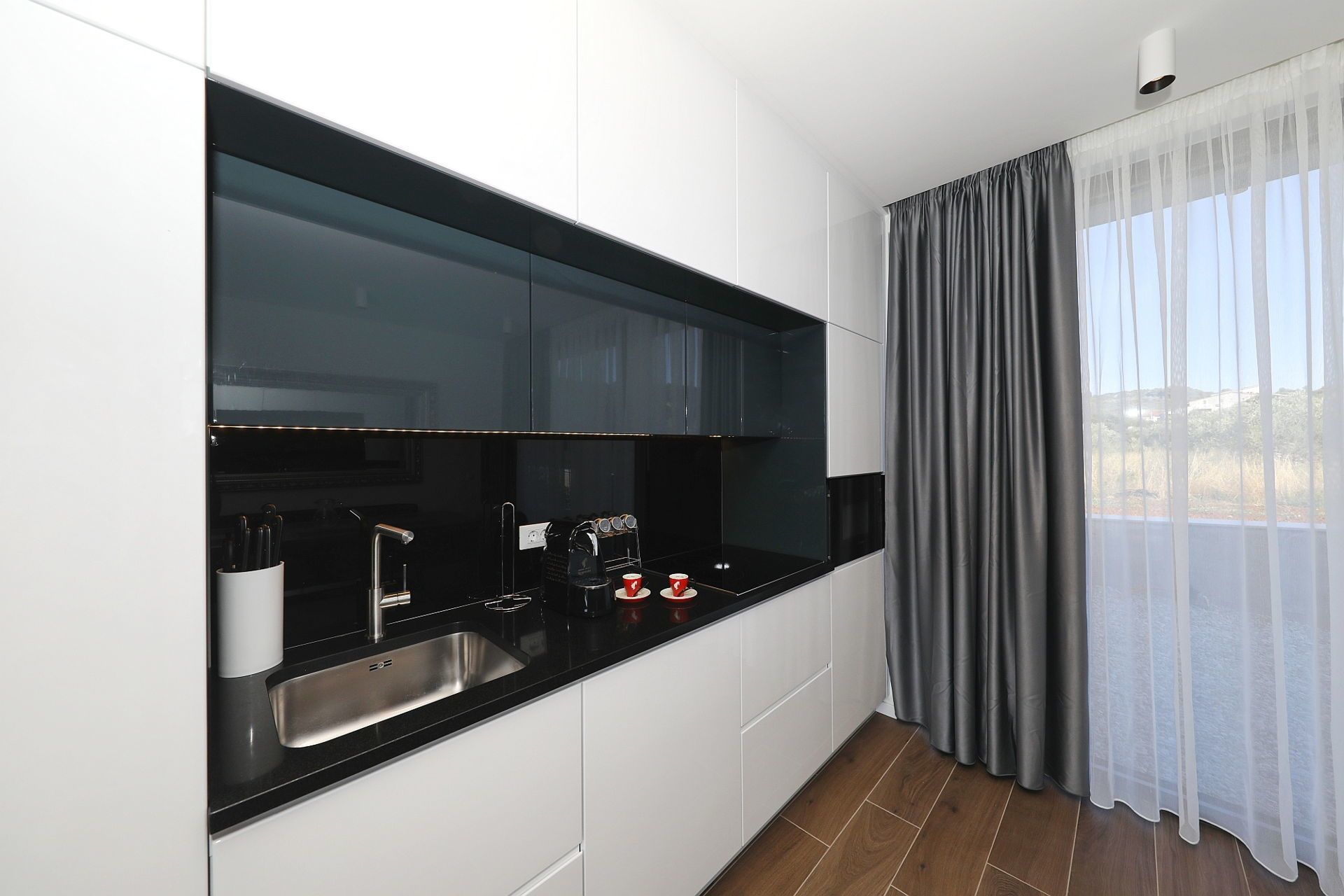 A modern kitchen with a black countertop, stainless steel sink, and white cabinets.