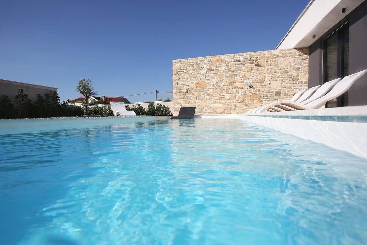 Una piscina con lettini e un muro in pietra.