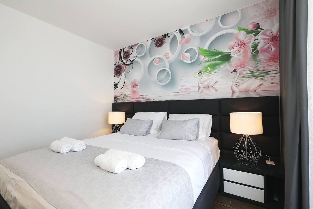Una camera d'albergo con un letto, due comodini con lampade e un grande murale floreale al muro.