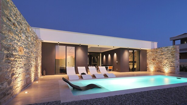 Zona de piscina moderna al aire libre con sillones de descanso y un muro de piedra.