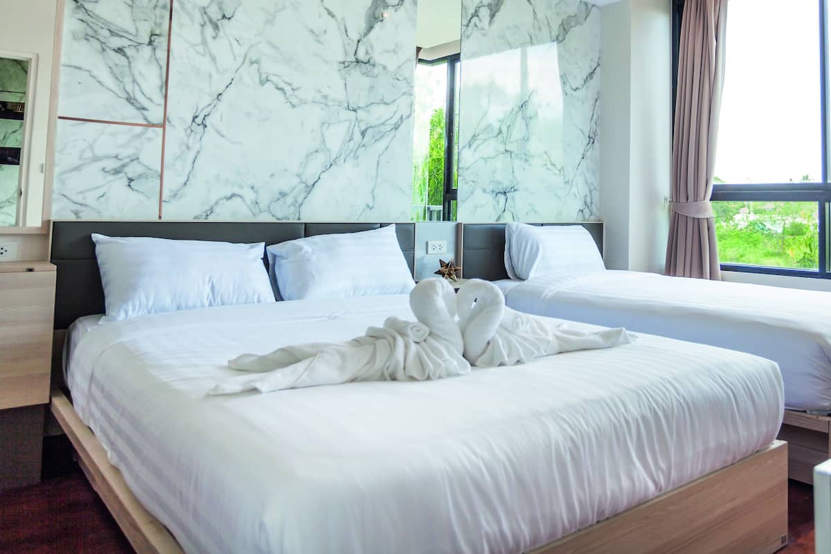 Een hotelkamer met twee bedden, een marmeren wand, een groot raam en een opgemaakt bed met een handdoek.