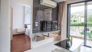 Ein modernes Wohnzimmer mit Flachbildfernseher an einer Marmorwand, einem Glastisch und einem Balkon mit Gartenmöbeln.