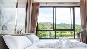Ein Hotelzimmer mit einem großen Bett, weißen Leinen und Blick auf eine üppige, grüne Landschaft durch ein großes Fenster.