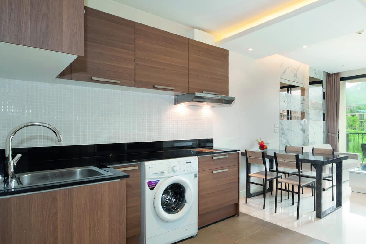 Een moderne keuken met een inbouw wasmachine, een eethoek met een glazen tafel, en uitzicht op een groen landschap door grote ramen.