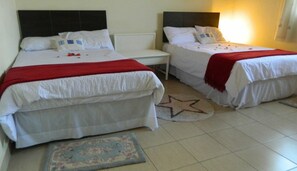 Ein Zimmer mit zwei Betten, jeweils mit weißer Bettwäsche und roten Wohndecken. Weiße Kopfteile sind vorhanden, und ein sternförmiger Teppich liegt auf dem Boden.