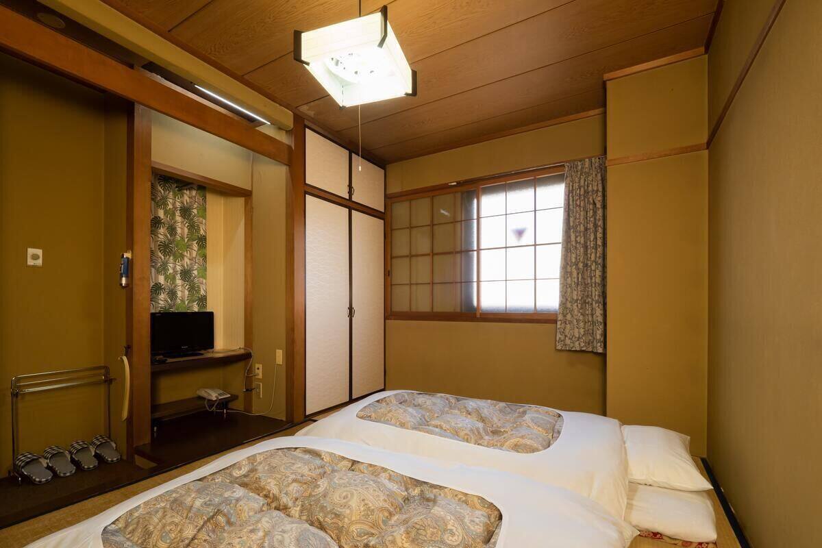 Een traditionele Japanse kamer met tatami vloeren, twee bedden met beddengoed met een patroon, een televisie en schuifdeuren.