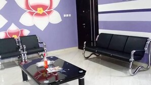 A waiting area with a black sofa, a glass-top table with a bottle, and a wall with a large flower design. - Dukusguest (Kumasi)