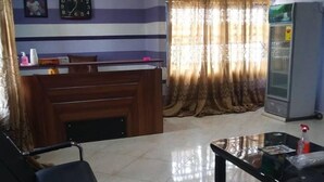 A reception area with a wooden desk, a black leather couch, a glass-top table, and a ceiling fan. - Dukusguest (Kumasi)