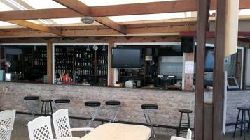 Een buitengebied met een bar, met een stenen muur, houten balken in het plafond en een flatscreen televisie boven de bar.