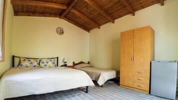 Un dormitorio con techo de madera, una cama con almohadas estampadas, una mesita de noche con lámpara, un armario y un refrigerador.