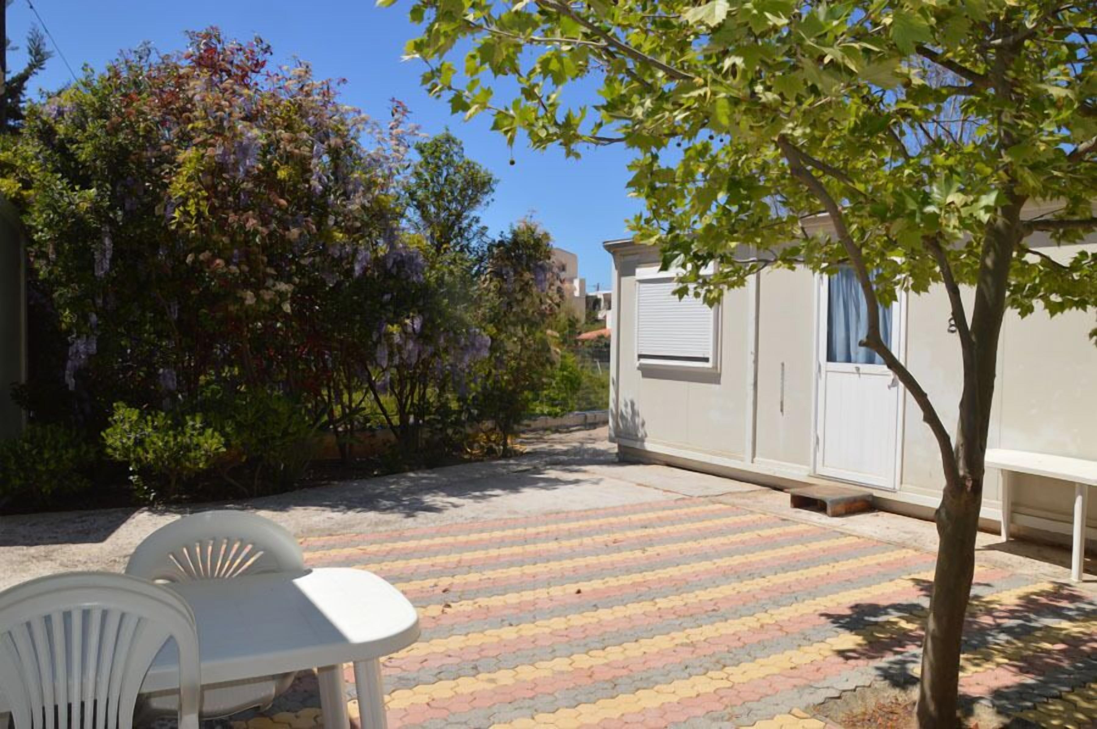 Une cour avec un sol carrelé, une table et une chaise blanches, et un arbre.