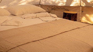 Una tienda de campaña con una cama, almohadas y un taburete de madera.