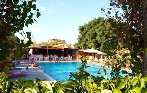 A pool area with lounge chairs and umbrellas, surrounded by greenery. - Camping Chania (Chania)