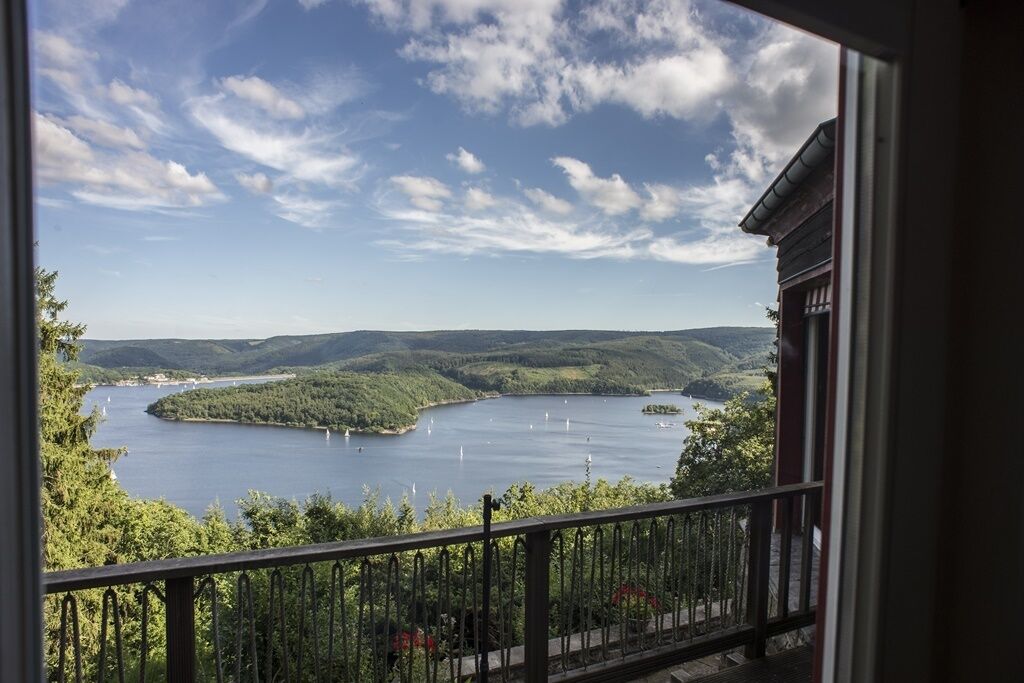 Une vue depuis un balcon donnant sur un lac, avec des collines environnantes et un ciel dégagé.
