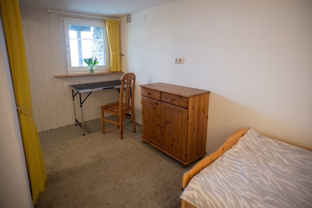 A bedroom with a bed, a desk, a chair, and a wooden wardrobe.