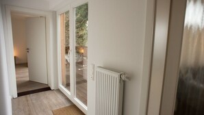 A hallway with a wooden floor, a white radiator, and a glass door leading to an outdoor area. - Holiday house "Waldhaus Anne" in Niedeggen - with a view of the Rursee (Nideggen)