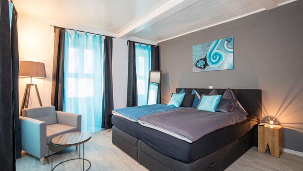 Un dormitorio moderno con una cama grande, una silla, una mesita de noche y un cuadro en la pared.
