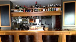 Zona de bar con mostrador de madera, varias estanterías llenas de botellas de licores, una exhibición de pasteles y taburetes de bar.