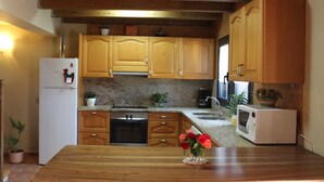 A kitchen with wooden cabinets, a white refrigerator, a microwave, and a wooden dining table. - Quiet and cozy house (Vilaplana la Baronia de Rialb Lleida)