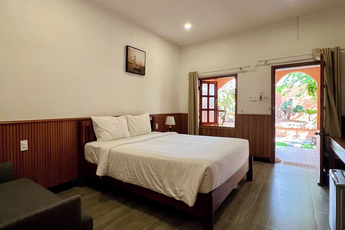 A hotel room with a bed, a desk, a chair, a window, and a door leading outside.