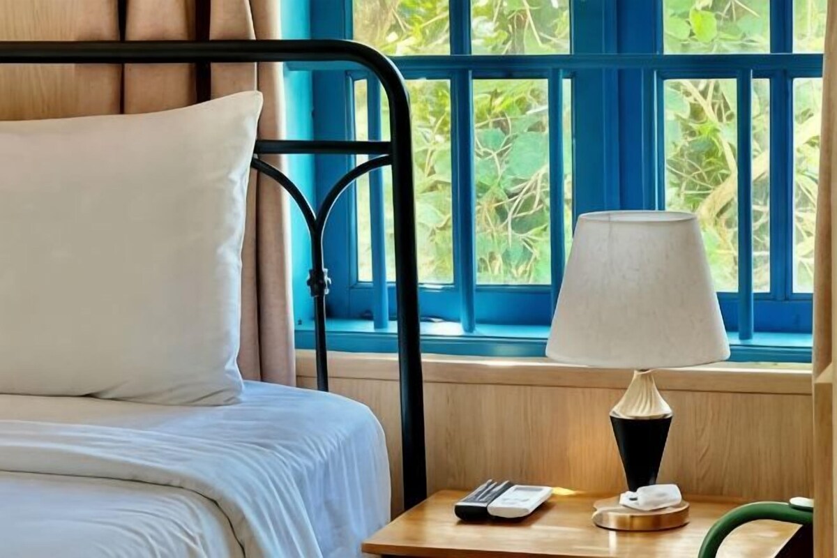 A bed with a white pillow, a bedside table with a lamp, a remote control, and a telephone.